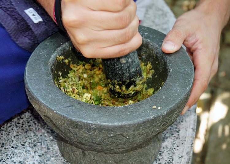 A woman mixing Thai green curry paste in a stone mortar