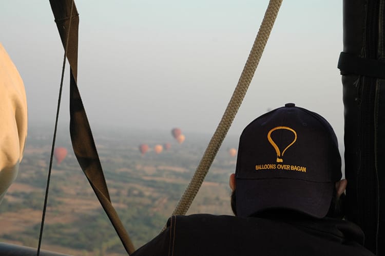 A person wearing a Balloons Over Bagan baseball cap looks out at the view from the hot air balloon