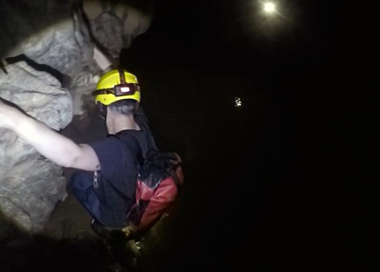 Neal climbs down some rocks to get to the river bank inside the cave