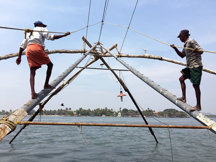 Two men walk up the poles to use their weight to lower the net back into the water at the Chinese fishing nets in Kochi