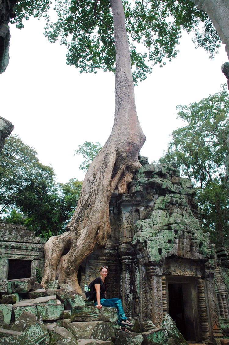 Michelle Della Giovanna from Full Time Explorer sits on the ruins of a temple with a giant tree growing over it