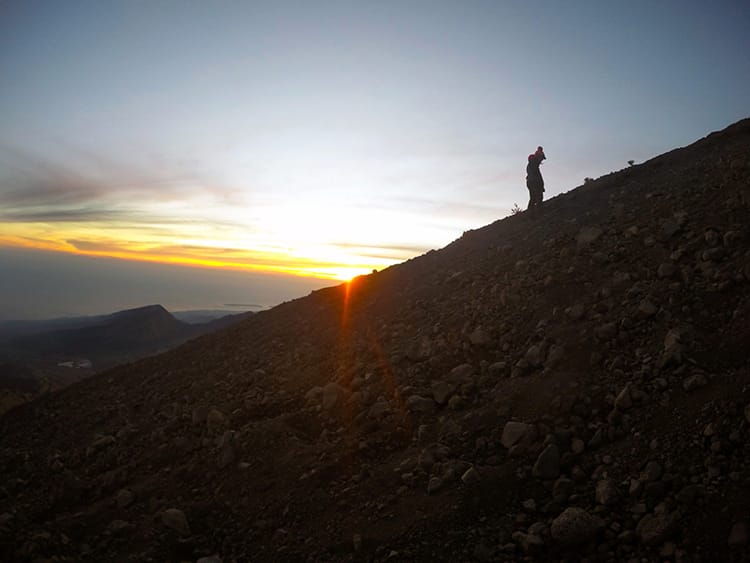 A single trekker climbs slowly up the dusty side of the volcano