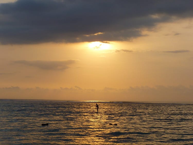 The sun setting over a paddle board in the ocean at Jungut Batu Beach in Nusa Lembongan