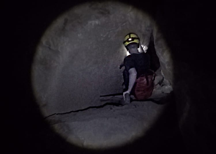 A man climbs through a small tunnel in a cave in Thailand