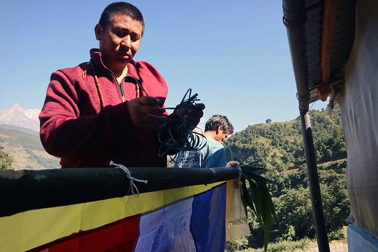 A monk blesses a flag pole with prayer flags to be raised in front of a teahouse for protection