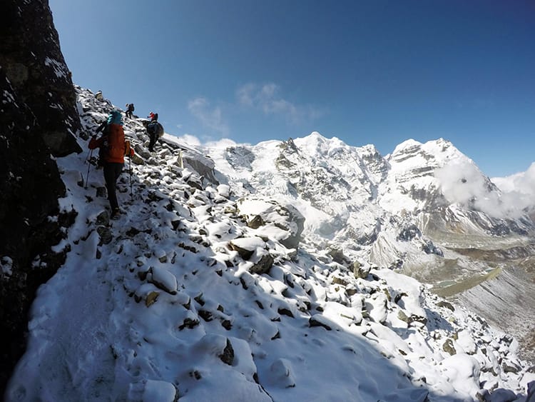 Trekkers climb a pile of rocks covered in snow