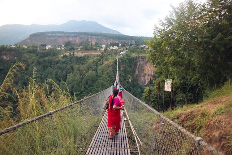 A woman wearing a red saree crosses a suspension bridge in Nepal