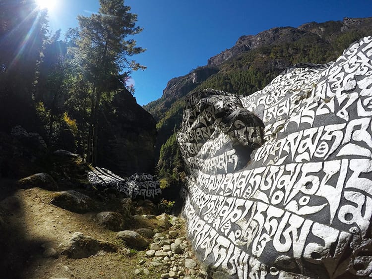 A large boulder rock painted place and white with the words Om Mani Padme Om repeated over and over