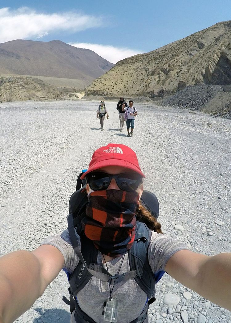 Michelle Della Giovanna from Full Time Explorer wears a buff, sunglasses, and hat on a windy day on the Annapurna Circuit