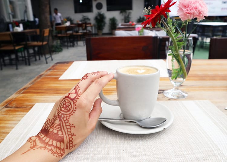 Michelle Della Giovanna from Full Time Explorer's hand decorated with henna while holding a coffee cup at Evoke Bistro
