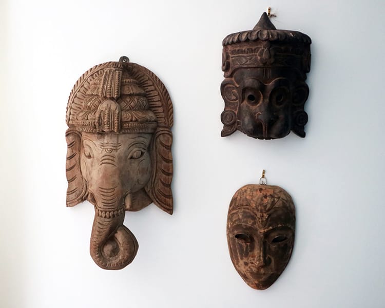 Three wood masks hung from the wall including Ganesh, Hanuman, and Buddha