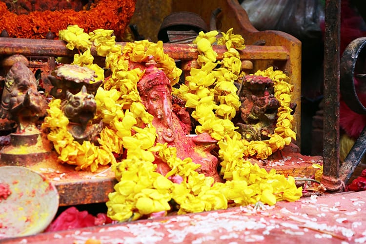 A Ganesh statue decorated with red sindoor powder and yellow flower garlands in Pharping