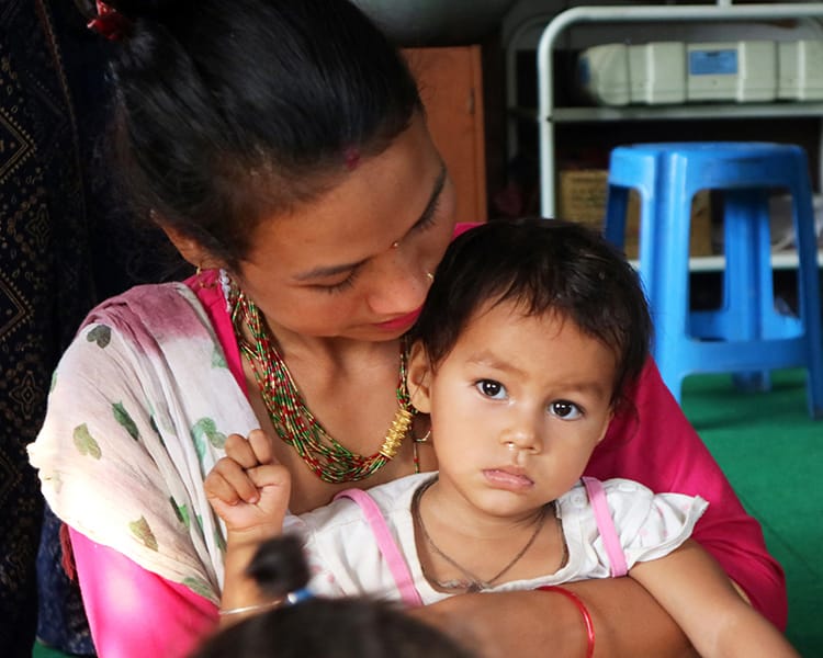 A women holds her daughter while waiting to see a physical therapist in Nepal