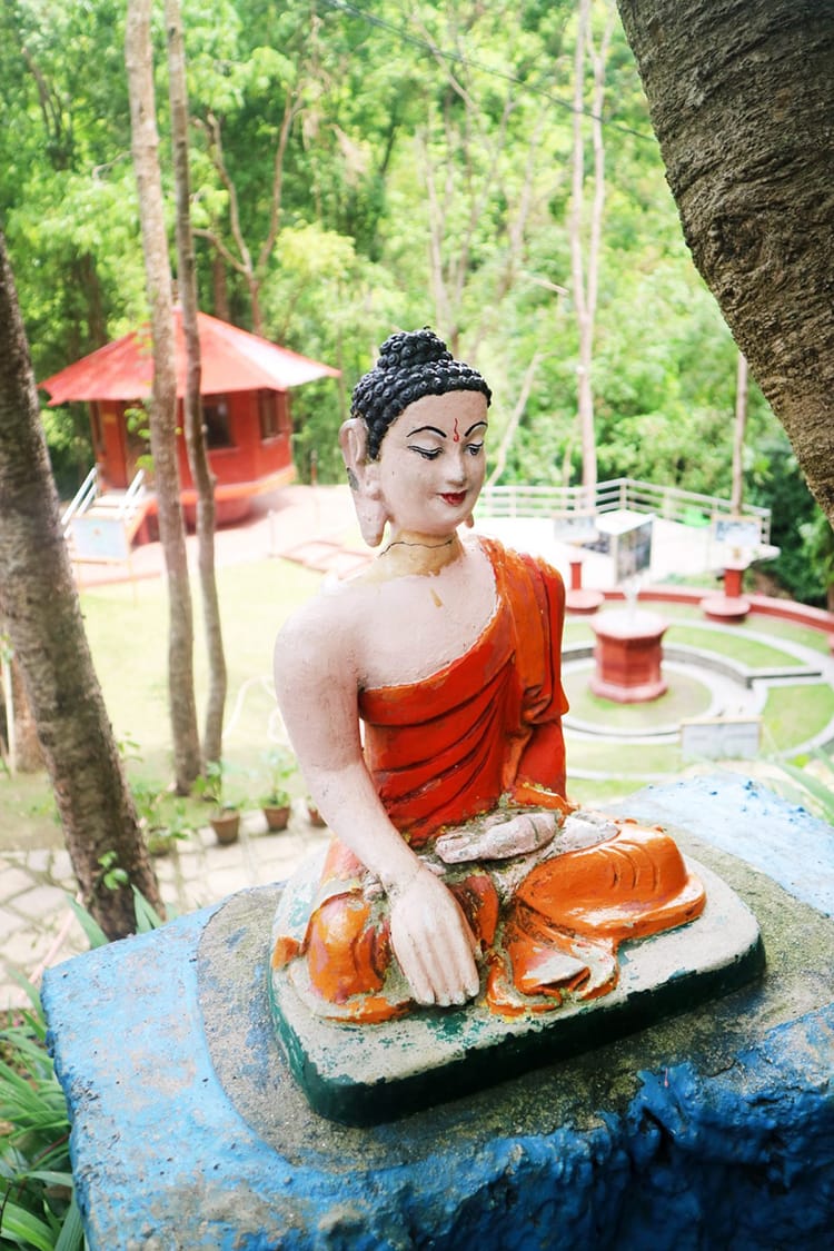 A buddha statue sits near a garden on the grounds