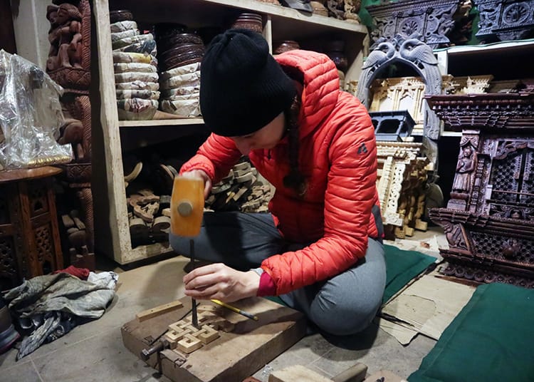 Michelle Della Giovanna of Full Time Explorer sits on the floor carving wood in a wood carving class