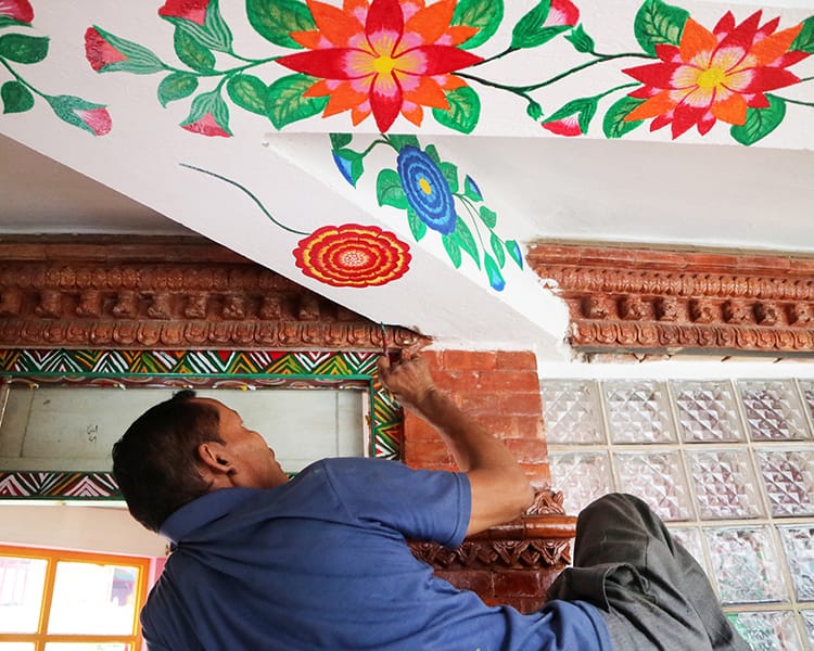 A man paints Mathili art on the ceiling in bright vibrant colors