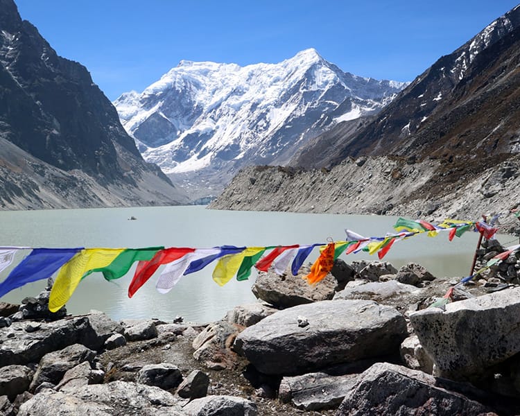 Prayer flags dance in the wind with Tsho Rolpa Lake and the Himalayan Mountains behind