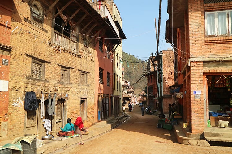 Women sit and chat on a street in Panauti, Nepal