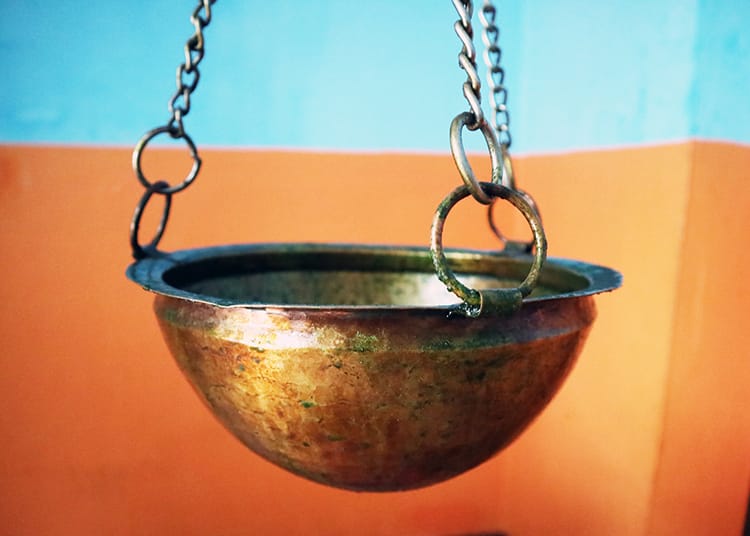 A brass bowl hangs from the ceiling for a Shirodhara treatment