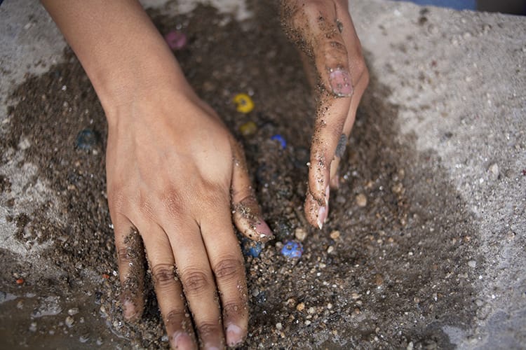 A woman rolls the beads in dirt to smooth them out