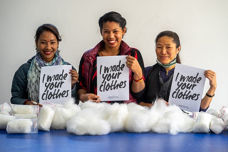 Three Purnaa employees holding signs that say I made your clothes