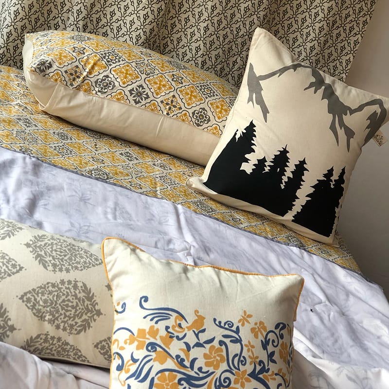 Bedding made by Cotton Mill Nepal featuring floral designs, french patterns, and a forest and mountain landscape in cream, gold, and gray