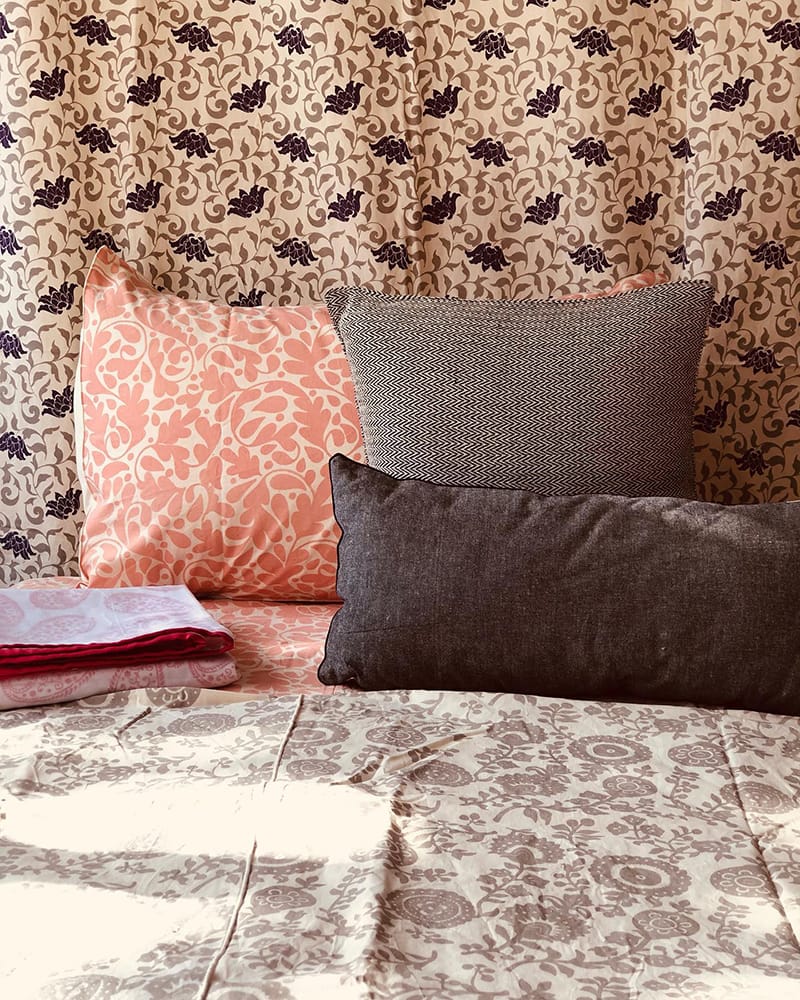 Bedding made by Cotton Mill Nepal featuring different floral prints in a salmon pink, eggplant purple, and medium gray