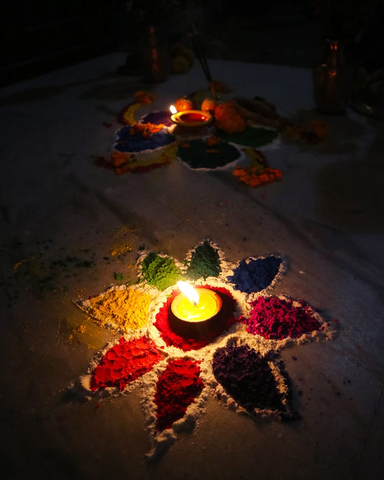 Two small rangoli mandala sit in front of a home on Laxmi Puja at night with candles glowing in the center