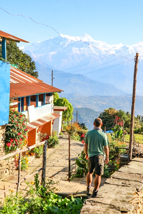Suraj stands in front of the village of Panchase Bhanjyang with the teahouse and himalayan mountains behind him