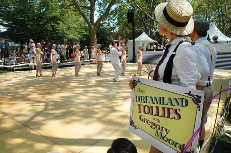 A woman holds a sign for the Dreamland Follies while they dance in the background