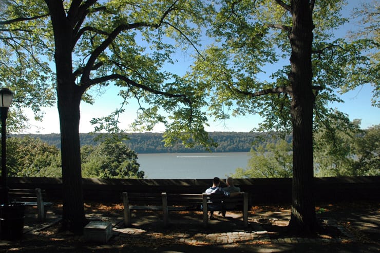 A couple sit on a bench looking out at the view of the Hudson River from Fort Tyron Park in Washington Heights