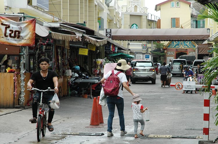 A woman holds a young childs hand while walking down a street in Bangkok