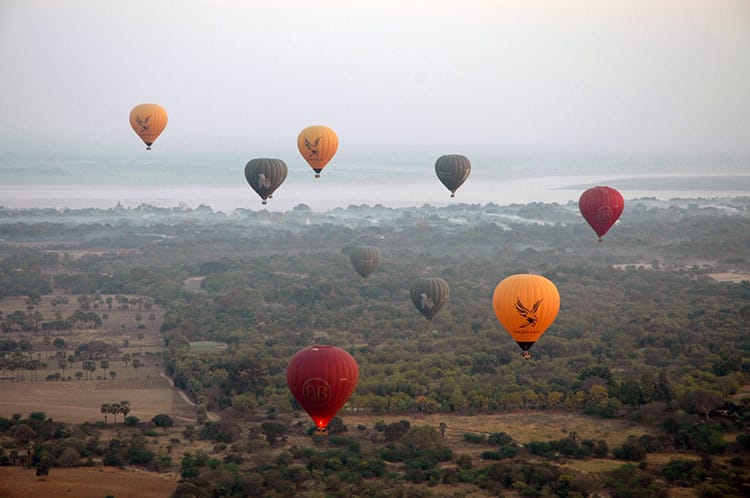 Red, yellow, and green hot air balloons fly over fields and temples in Bagan, Myanmar
