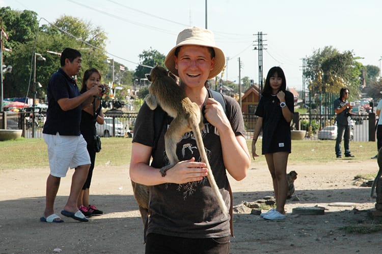 Neal stands in Lopburi, Thailand with a monkey climbing on his shoulder
