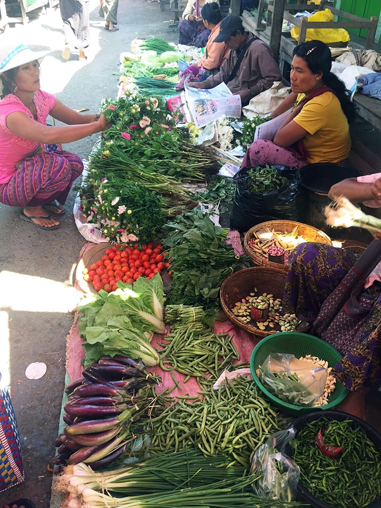 Women sit on the floor with blankets covered in vegetables for sale in front of them in the local market