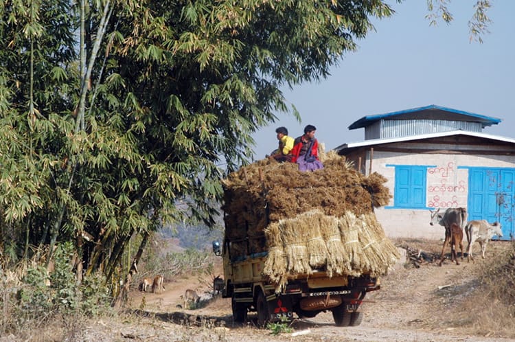 Two young men sit on top of a hay truck driving through Myanmar