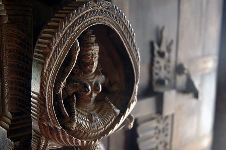 A handle to a door which is intricately carved out of wood with a person in the middle