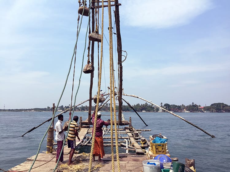 Three men pull a fishing net up in Fort Cochin