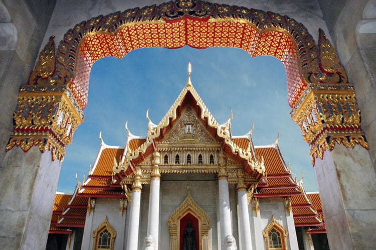 Elaborate temple entrance in Bangkok Thailand with red and gold trim