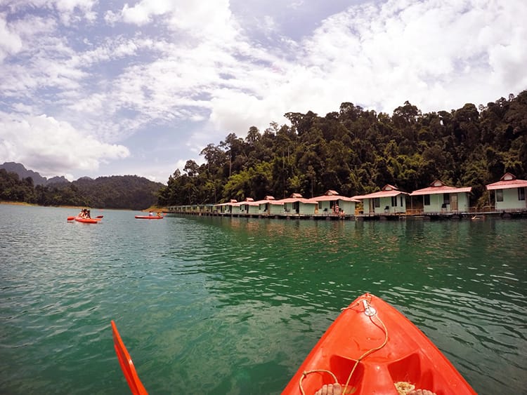 A bright orange kayak approaches the overnight huts in Khao Sok National Park