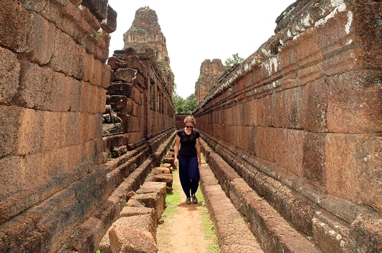 Michelle Della Giovanna from Full Time Explorer walks through the red stone walls outside on of the temples in Angkor Wat