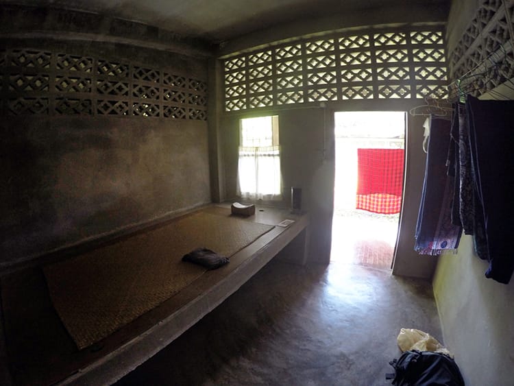 A cement bed and wood pillow in a cement room at a silent meditation retreat in Thailand