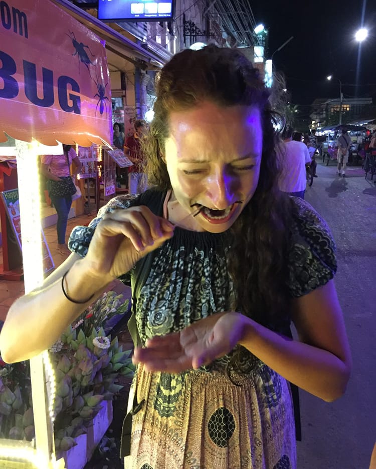 Michelle Della Giovanna from Full Time Explorer cringes as she eats a tarantula in Siem Reap