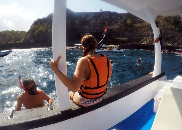 Michelle Della Giovanna from Full Time Explorer sits at the edge of a boat wearing a snorkel and life jacket before jumping into the water