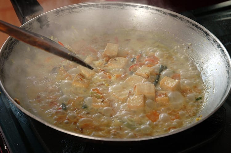 Cooking the tofu curry in a coconut cream sauce in a giant wok pan