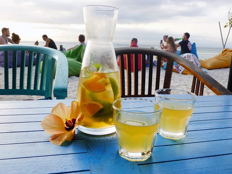 A bottle of white sangria and two glasses sit on a table as the sun sets in Bali