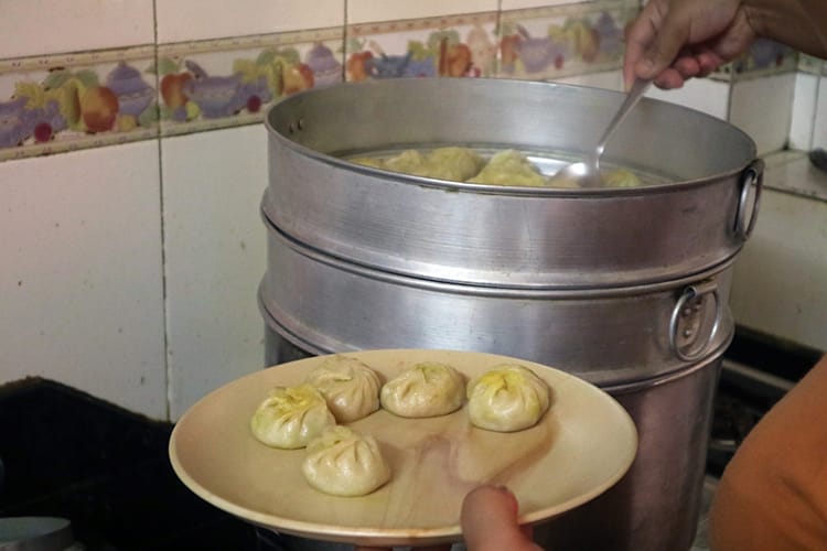 Cooked momos being taken out of a steamer and put on a plate