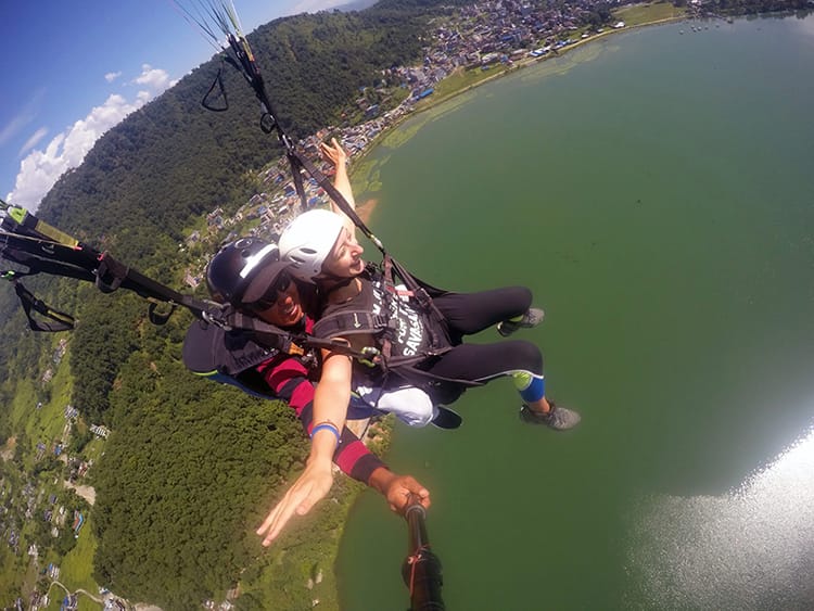 Michelle Della Giovanna from Full Time Explorer paragliding through the air above Lake Phewa in Nepal