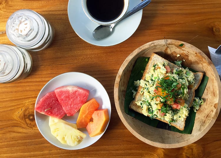 Fresh fruit, scrambled eggs on toast and a coffee served for breakfast at a homestay