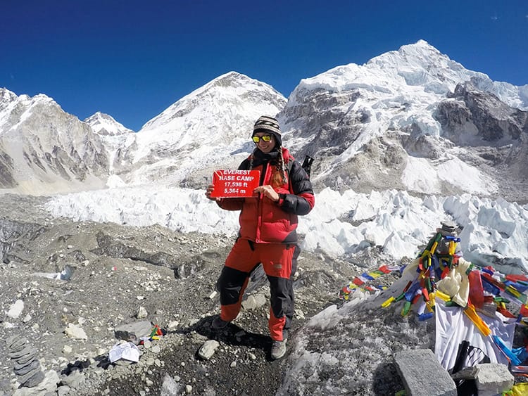 Michelle Della Giovanna from Full Time Explorer holds the red Everest Base Camp sign on a clear day